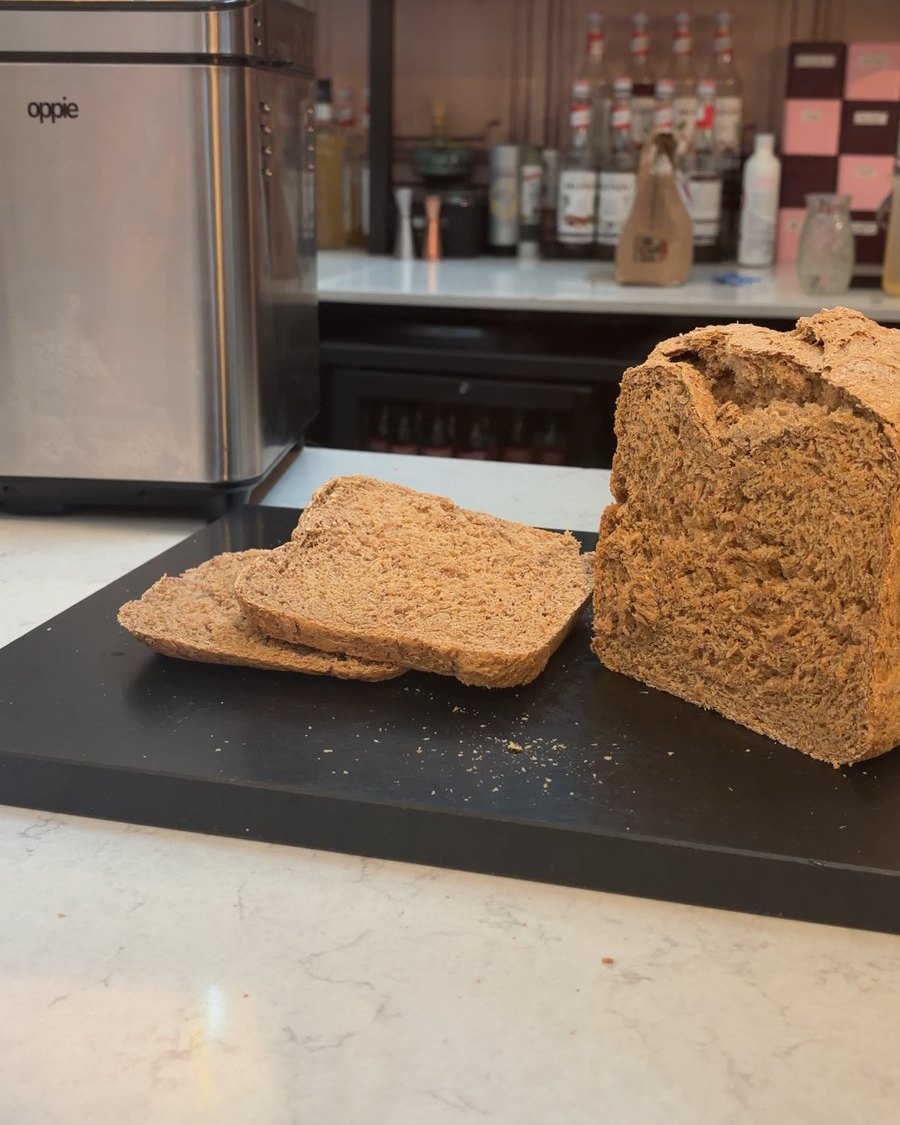 Zelfgebakken volkorenbrood, aangesneden op een snijplank naast de Oppie-broodbakmachine